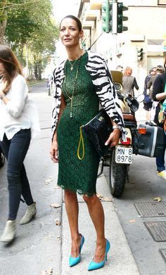 a woman in a green dress and zebra print jacket is walking down the street with her handbag