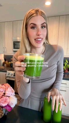 a woman holding a green drink in her hand and pointing to it with the caption