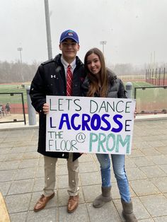 a man and woman standing next to each other holding a sign that says let's dance across the floor or prom