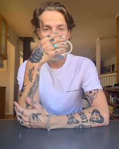 a man sitting at a table with tattoos on his arms and hands, drinking from a cup