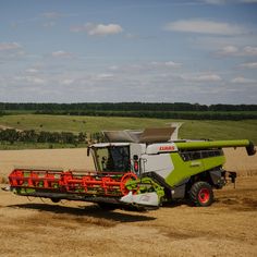 a green and white combine is in the middle of a field with red bales