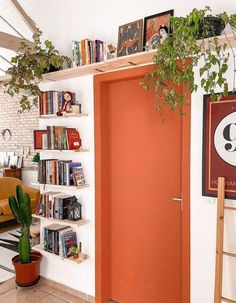 an orange door in a white room next to a book shelf with books on it