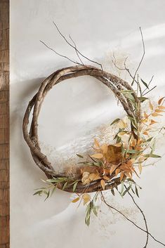 a wreath made out of branches and leaves hanging on a wall with a white background