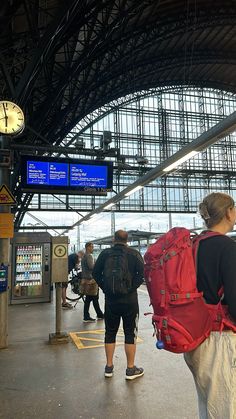 two people with backpacks are walking through the train station while another person is waiting