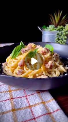 a bowl filled with pasta and sauce on top of a table next to a potted plant