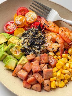 a bowl with shrimp, avocado, corn and tomatoes on the side next to a fork