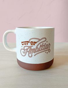 a white and brown coffee cup sitting on top of a wooden table next to a pink wall