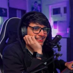 a young man wearing headphones sitting in front of a microphone and computer keyboard, smiling at the camera