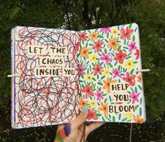 a hand holding up an open notebook with writing on the pages and flowers around it