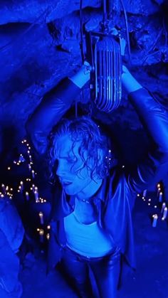 a woman in leathers holding up a cage over her head with blue lights around her