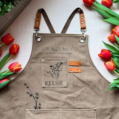 a brown apron with flowers on it sitting next to tulips and green leaves