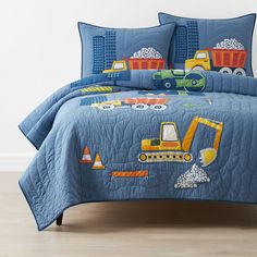 a blue quilted bed with construction vehicles on it and matching pillow shampoos