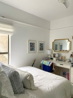 a white bed sitting under a window next to a desk with a mirror on it