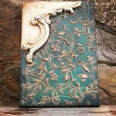 an ornately decorated book sitting on top of a wooden table next to a stone wall