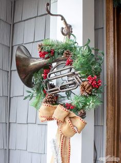 a christmas wreath hanging on the side of a house with an old horn and pine cones