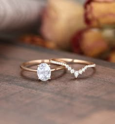 two gold rings with white stones on them sitting on a wooden table next to flowers