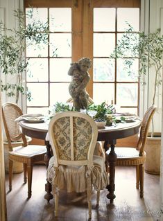 a teddy bear sitting on top of a table in front of a window with chairs around it