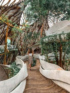 a woman walking down a wooden walkway surrounded by trees and greenery in a building