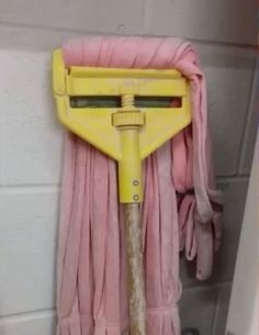 a yellow dust mop hanging on the side of a shower wall next to a pink towel