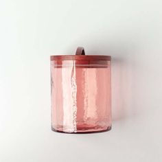 a pink glass jar hanging on the wall next to a white wall with a wooden lid