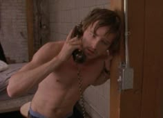 a shirtless man holding a phone to his ear while standing in front of a door