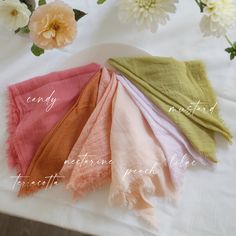 four different colored scarves sitting on top of a white plate with flowers in the background