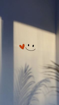 an image of a window with a smiley face drawn on the glass and palm leaves behind it