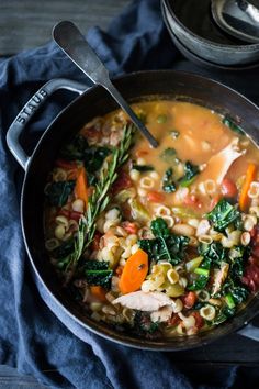 a pot filled with pasta and vegetables on top of a blue cloth next to a spoon