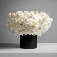 a black vase filled with white flowers on top of a table