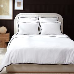 a white bed with black trim and two pillows on it's headboard in a bedroom