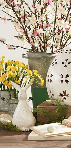 some white vases with flowers and books on a table