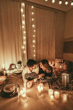 a man and woman sitting on top of a bed next to each other in front of candles