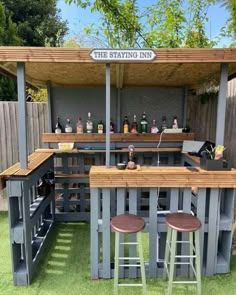 an outdoor bar made out of pallets with stools in the grass and some bottles on top