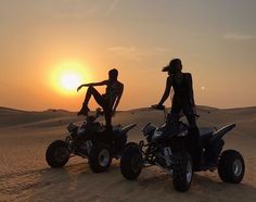 two people on four wheelers in the desert at sunset or dawn, with one person standing behind them