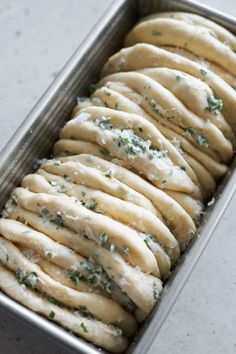 a metal pan filled with sliced bread covered in white cheese and green herb toppings