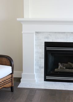 a white fireplace with a black mantle and chair