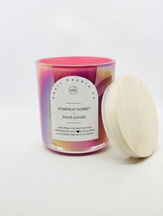 a candle next to a wooden lid on a white surface with a pink and purple design