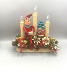 an elf sitting on top of a christmas decoration with candles and decorations around him,