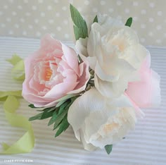 two pink and white flowers sitting on top of a striped table cloth with green leaves