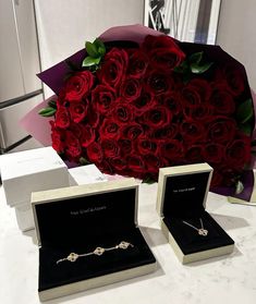 a bouquet of red roses in a white box and two necklaces on a table