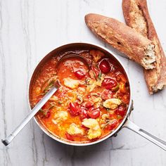 a bowl filled with soup next to bread on top of a white countertop and two spoons