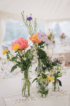 three vases filled with flowers sitting on top of a white tablecloth covered table