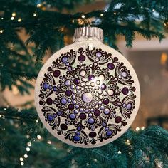 an ornament hanging from a christmas tree decorated with purple and white designs on it