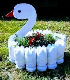 a white swan made out of plastic bottles is sitting in the grass next to some plants