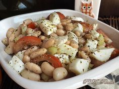 a white bowl filled with beans and veggies next to two oranges on a table