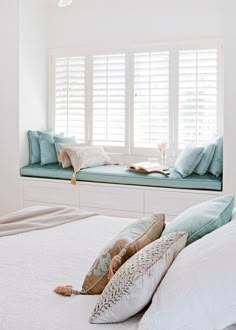 a bedroom with white walls and pillows on the bed, along with a window seat