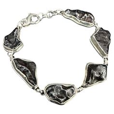 Six roughly 10 x 22 mm fragments of the Sikhote-Alin Meteorite are held in thick handmade sterling silver bezels with double bezel accents below, and linked, to create this unique "otherworldly" bracelet highlighting these visitors from the cosmos. These iron-nickel meteorite(s) fell over a 100 kilometer radius in southeastern Russia's Sikhote-Alin Mountains in 1947. Meteorite falls had been witnessed and fragments recovered before, but never of this magnitude. An estimated 23 tons reached ground. Each fragment shows a "fusion crust' indicative of its flaming entry in the atmosphere. The 7 1/2 inch length of the bracelet fits most wrists, and also is adjustable towards smaller wrists utilizing the jump rings. Out of this world! Fall Over, Iron Meteorite, Meteorite Ring, Modern Bracelets, Out Of This World, Jump Rings, Handmade Sterling Silver, Cosmos, Sterling Silver Bracelets