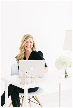 a woman sitting at a desk with a laptop computer in front of her and a house model on the table