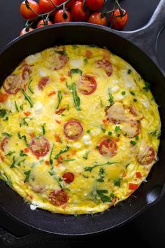 an omelet with tomatoes and spinach in a skillet on a table