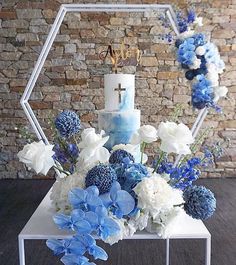 a blue and white wedding cake with flowers in front of a brick wall behind it